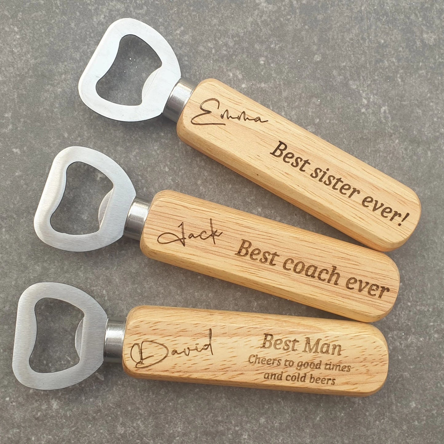 Three wooden bottle openers with engraved text on a gray surface