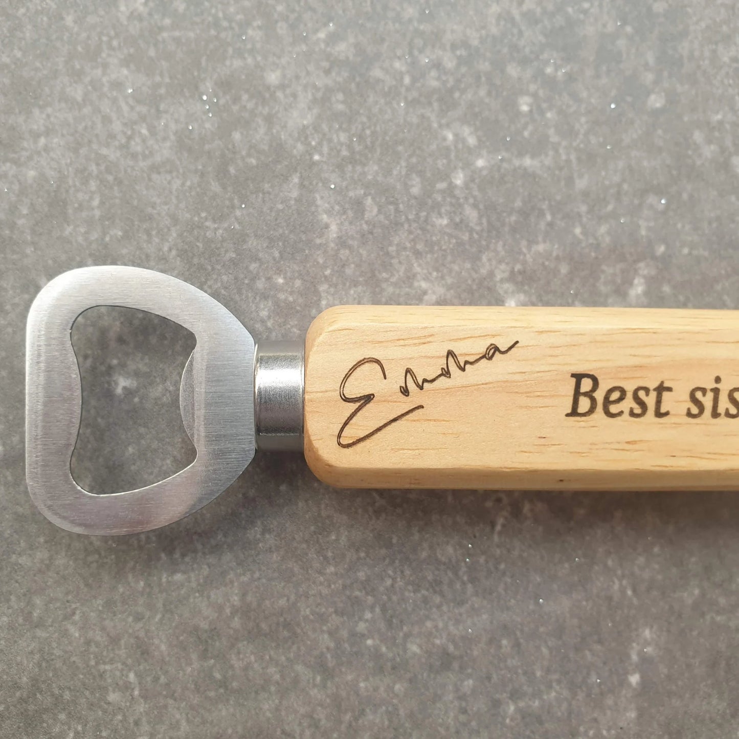 Bottle opener with wooden handle and engraved text on a gray surface
