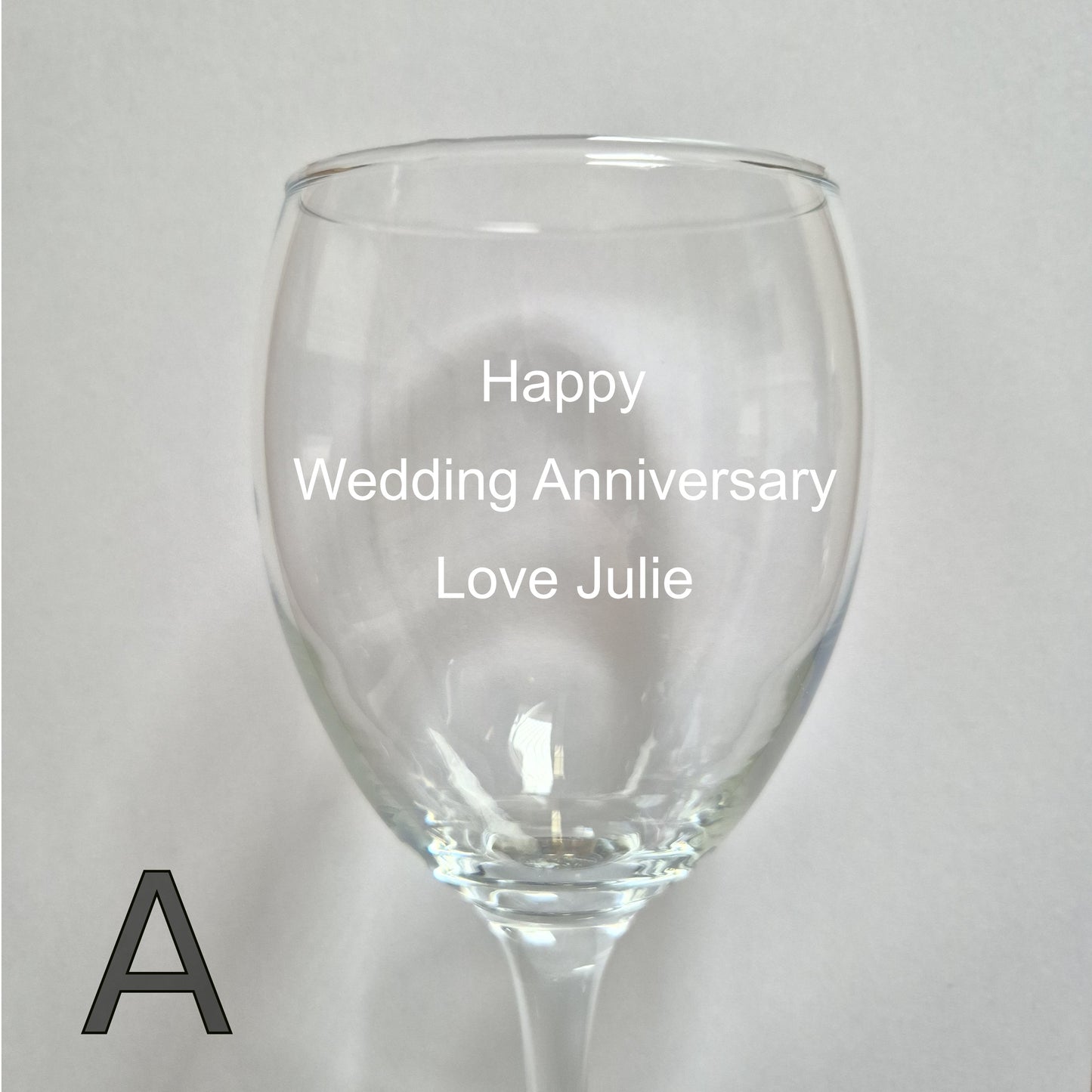 Personalised wine glass with 'Happy Wedding Anniversary Love Julie' text on a light gray background