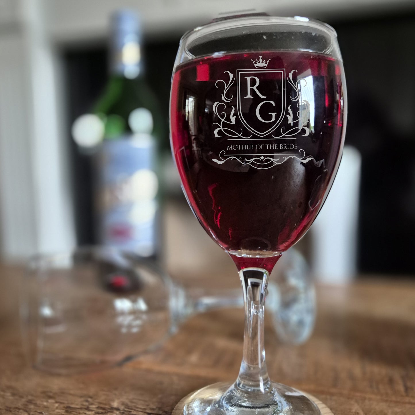 personalised wine glass with logo engraved on the front. glass is filled with red wine on a wooden table.