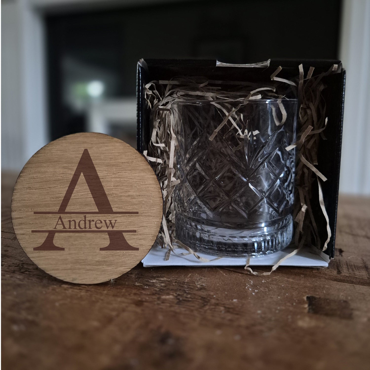 Personalised whisky glass sat on a wooden table with an oak coaster. The coaster has an A mongrame and name engraved on it.