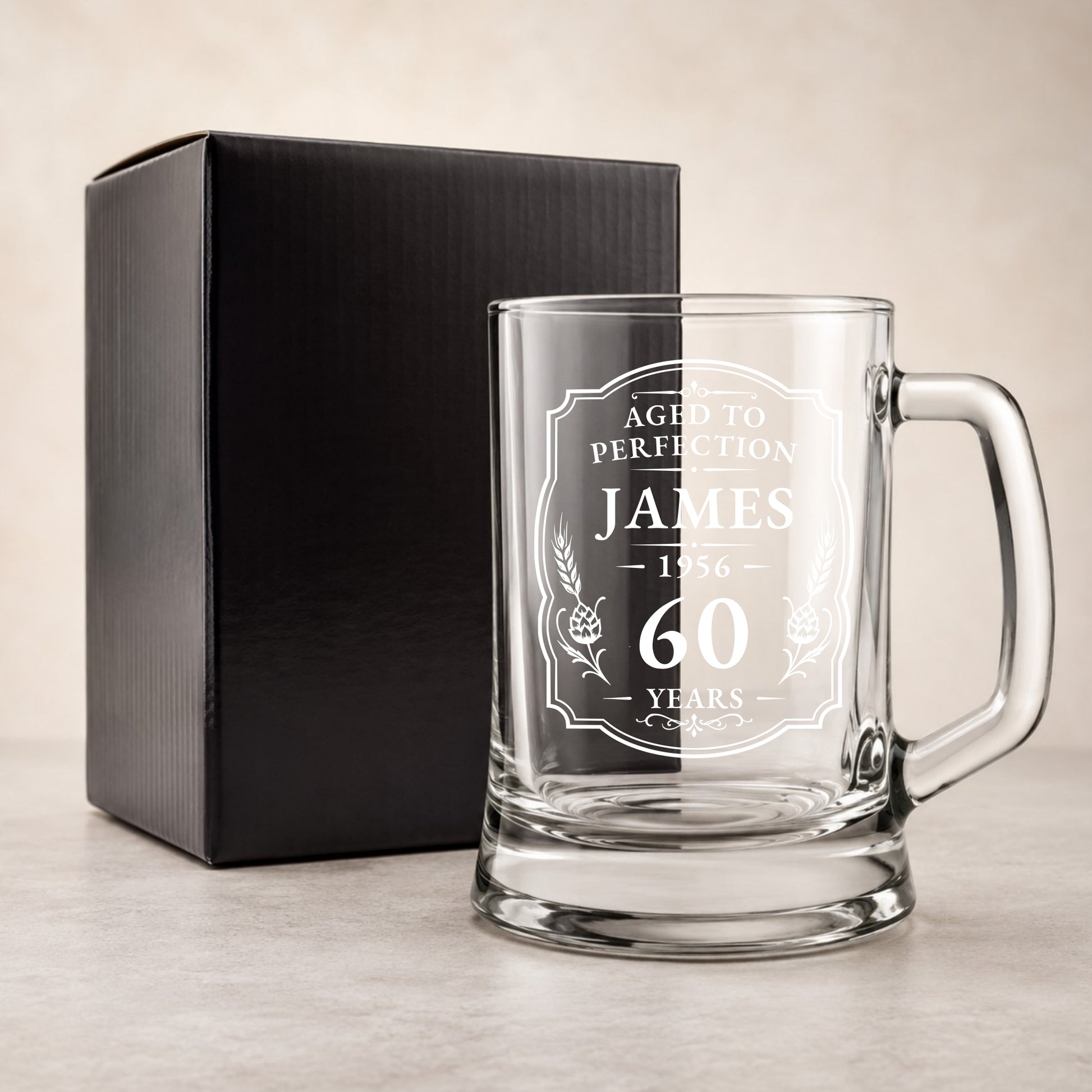 Clear glass mug with engraved text and a black gift box on a beige background