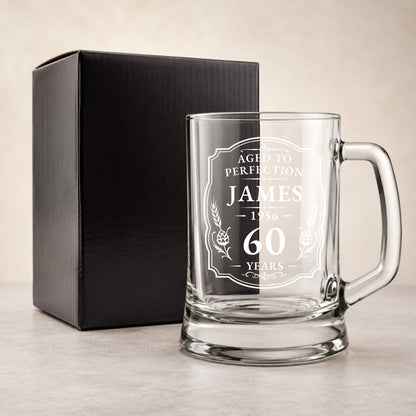 Clear glass mug with engraved text and a black gift box on a beige background