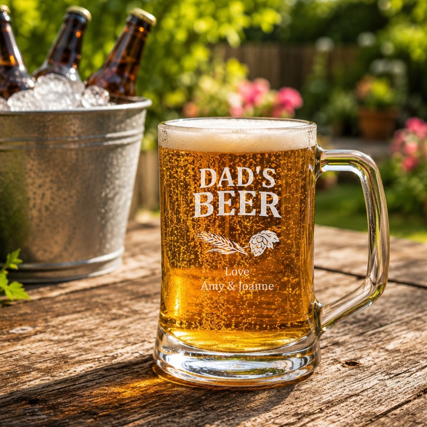 Glass mug of beer with 'DAD'S BEER' engraving on a wooden table outdoors.