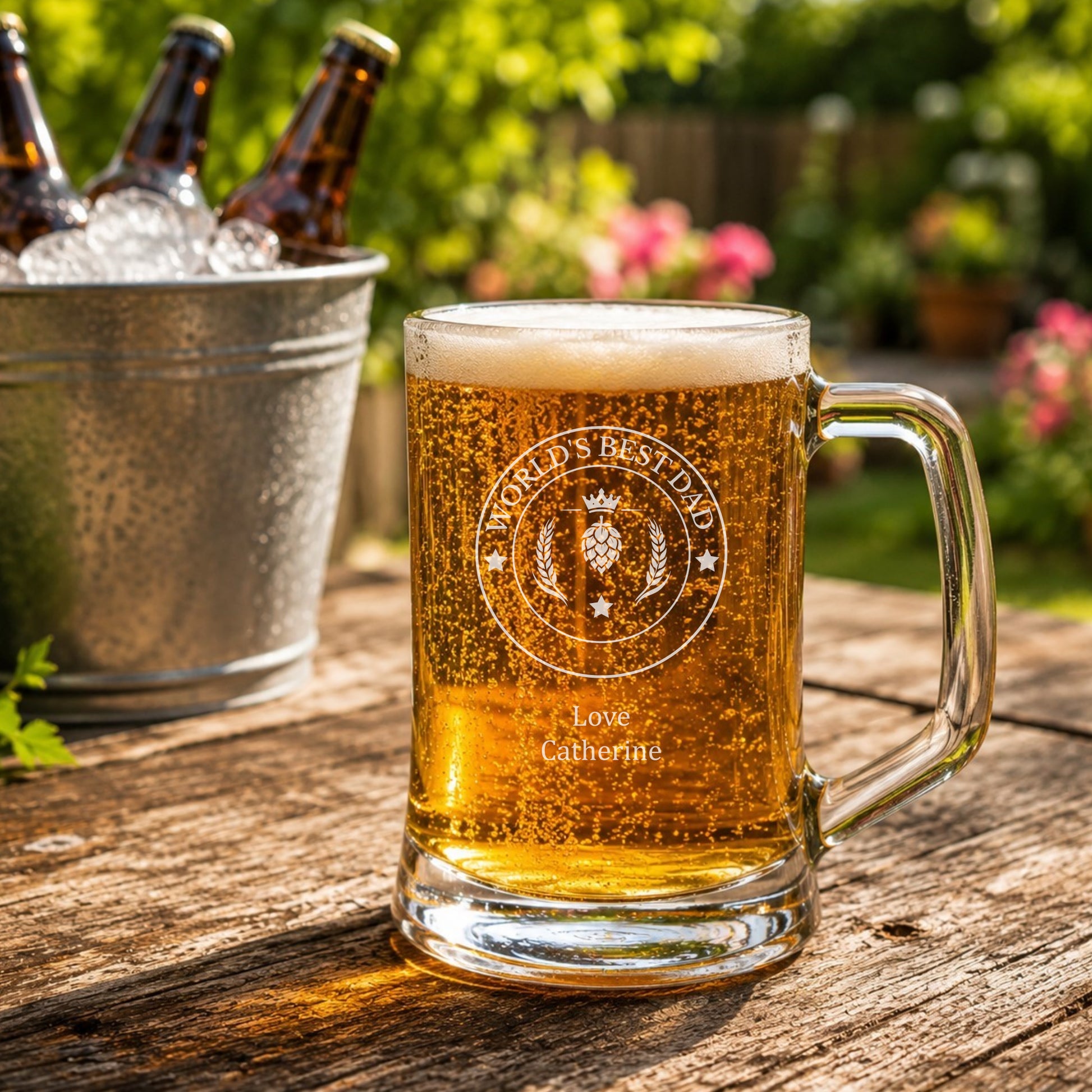 Glass of beer with 'World's Best Dad' engraving on a wooden table outdoors.