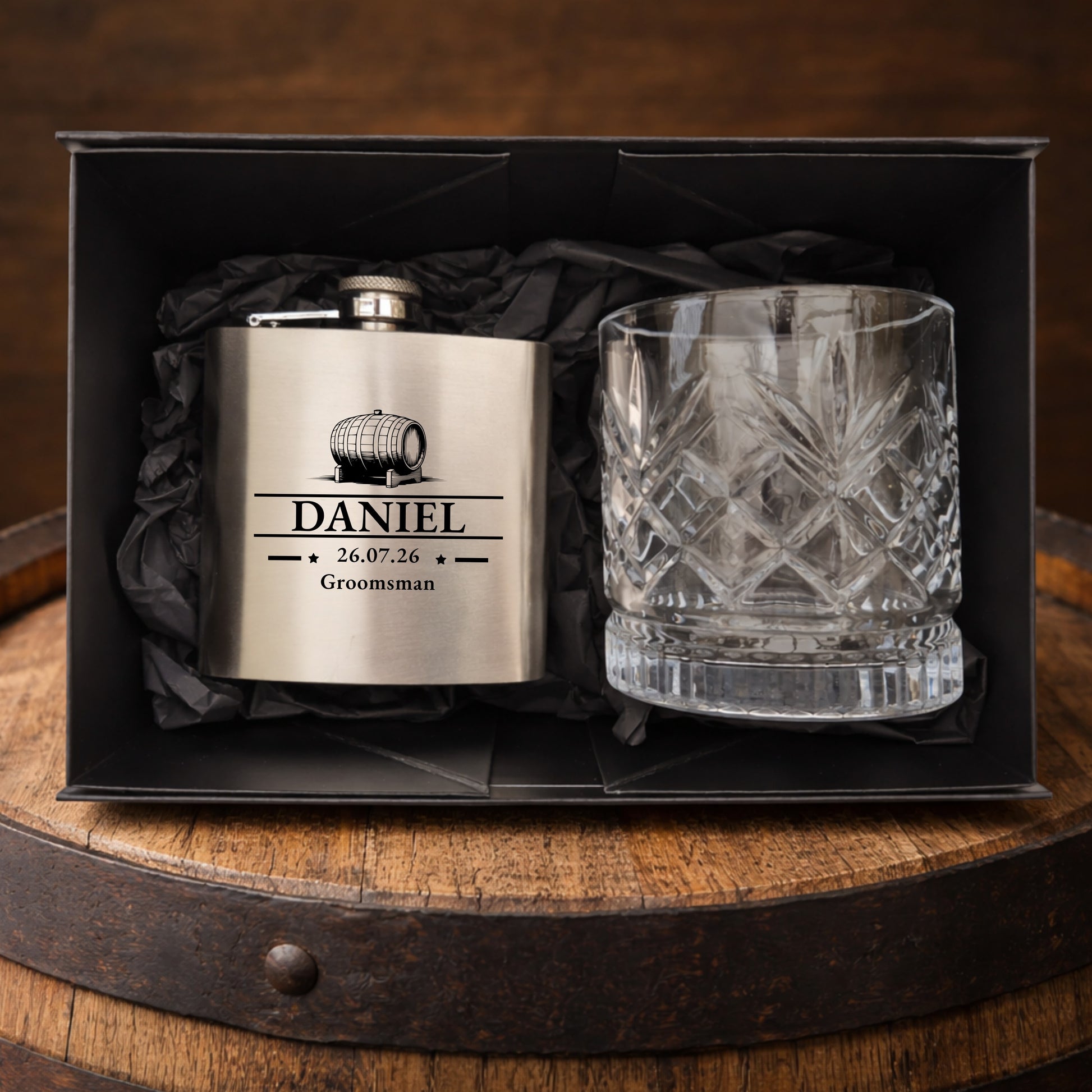 Personalized flask and glass set in a black box on a wooden barrel.
