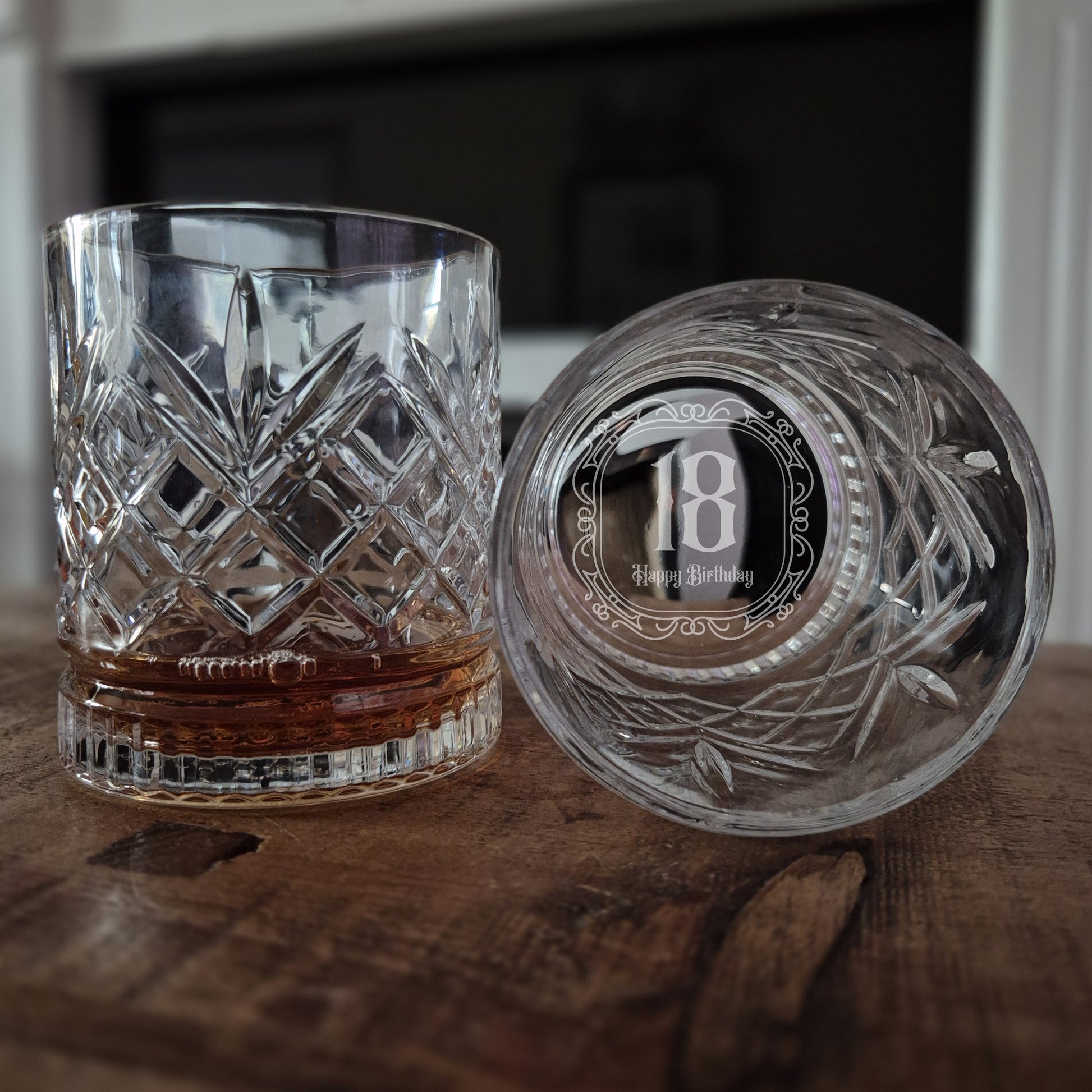 Two crystal glasses on a wooden surface, one with an engraved number 18.