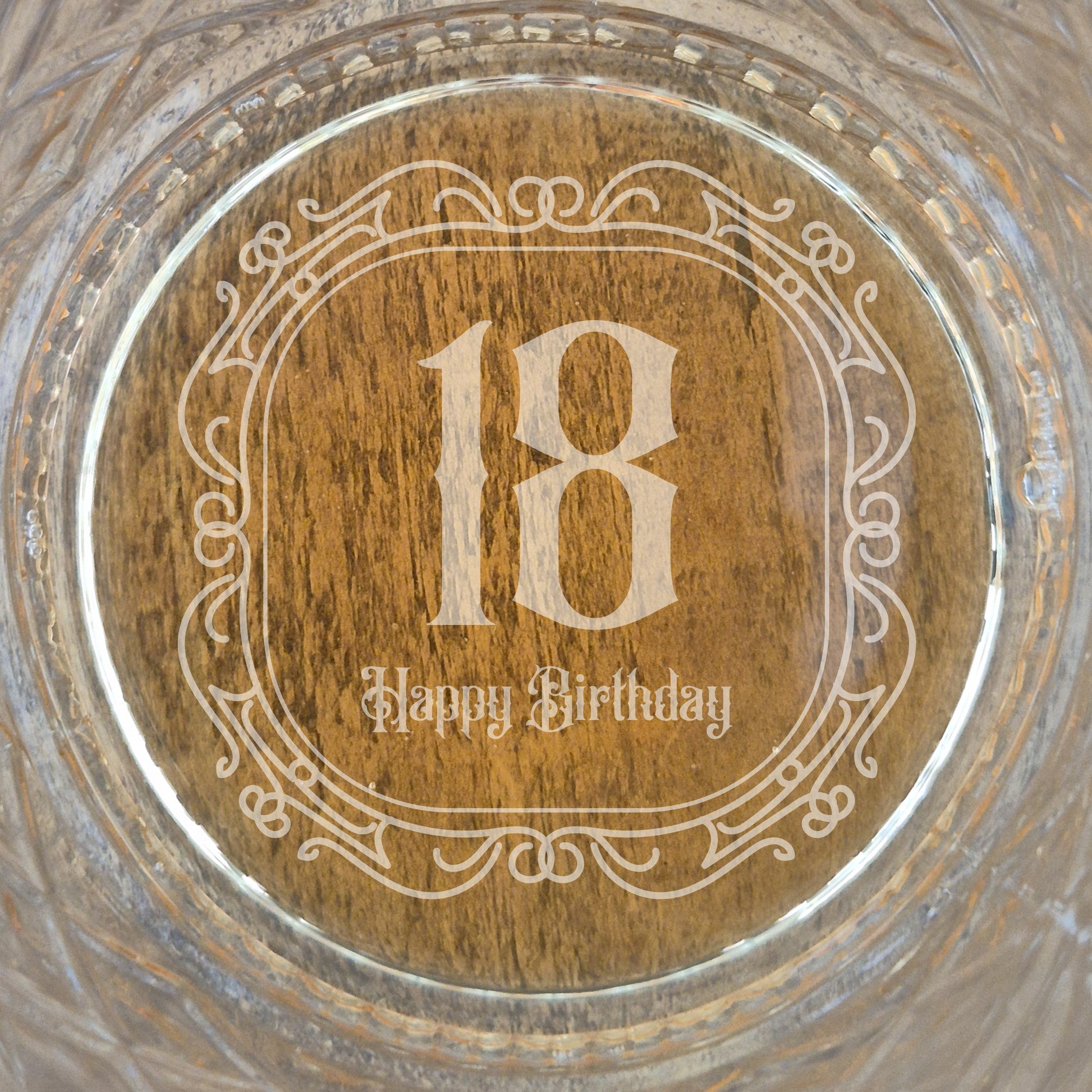The base of a personalised whisky glass with '18 Happy Birthday' engraving on a glass surface