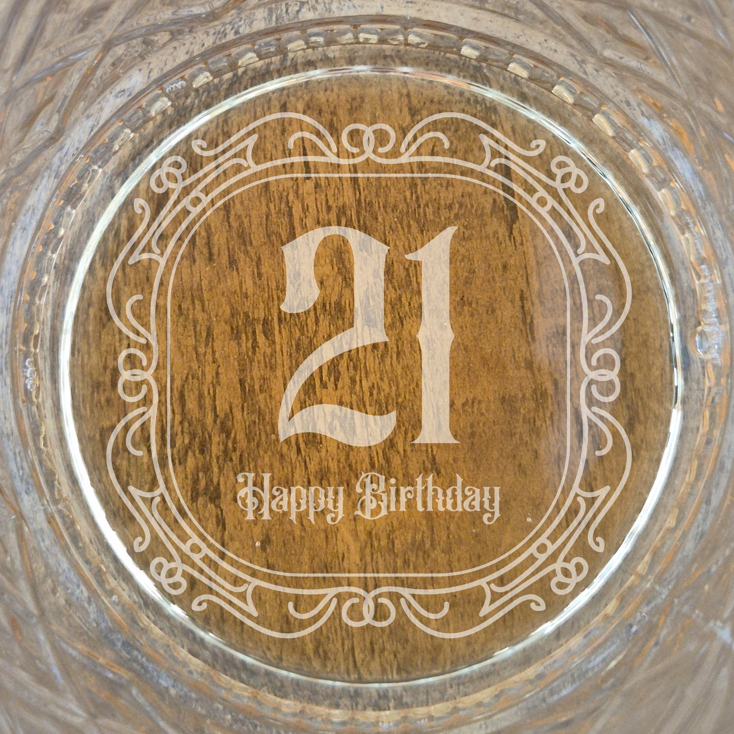 The base of a personalised whisky glass with '21 Happy Birthday' engraving on a glass surface