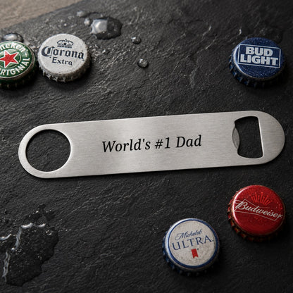 Bottle opener with 'World's #1 Dad' engraving on a dark surface with beer bottle caps.