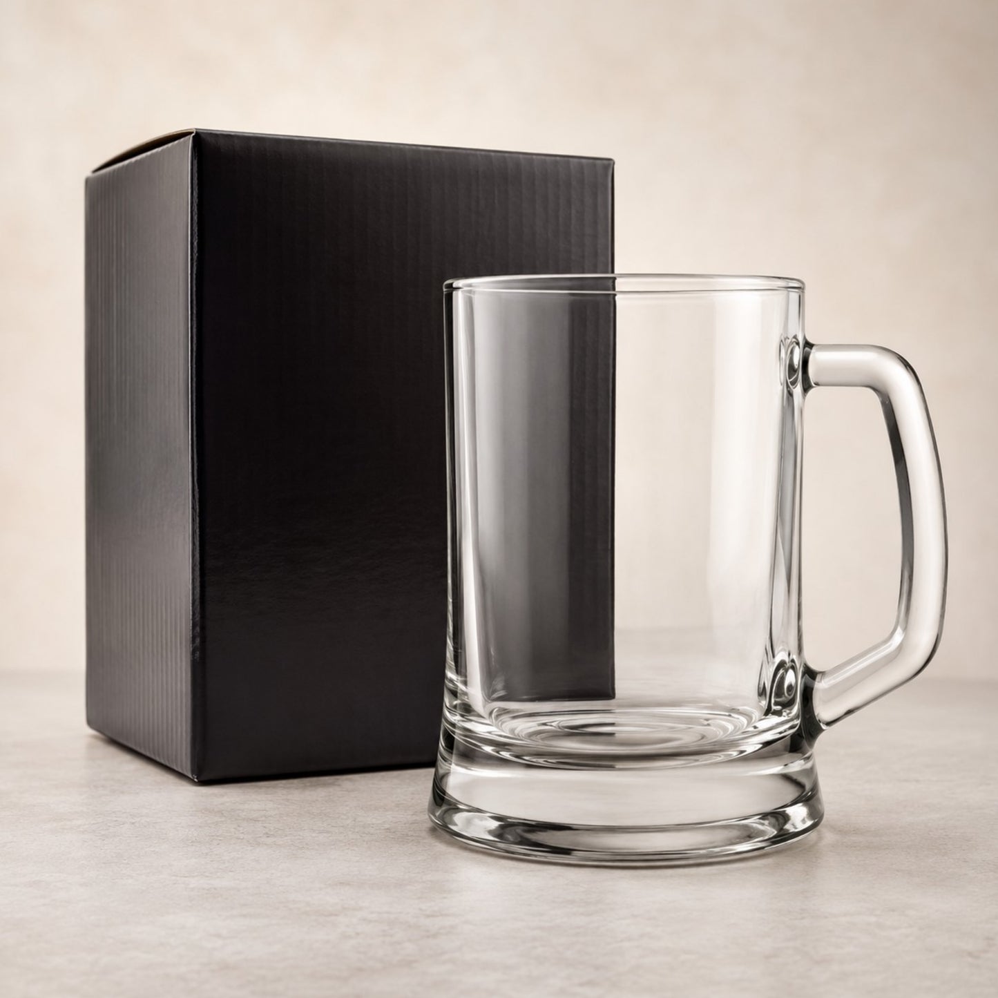 Clear glass mug with handle next to a black box on a light background