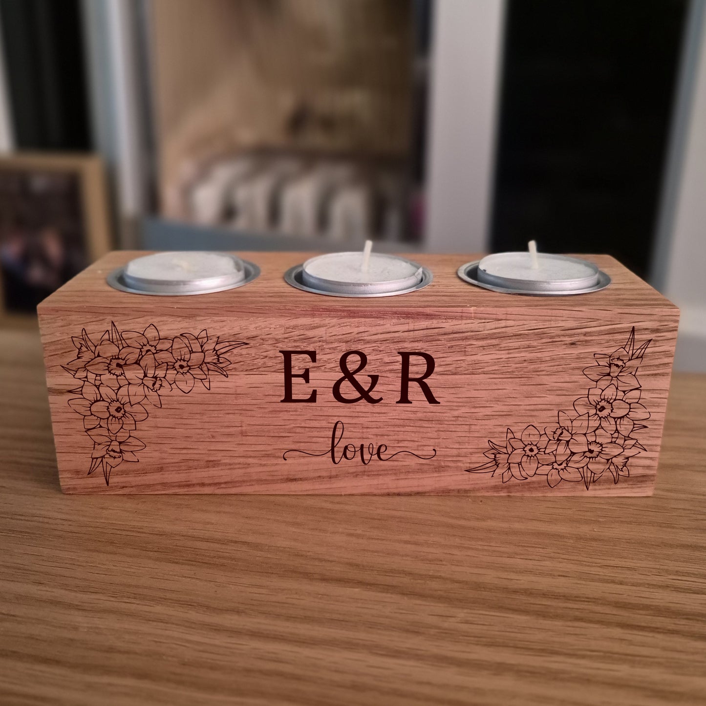 Oak tealight candle holder with engraved initials 'E&R' and flowers on a wooden surface.