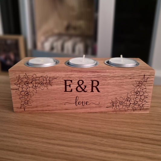 Oak tealight candle holder with engraved initials 'E&R' and flowers on a wooden surface.