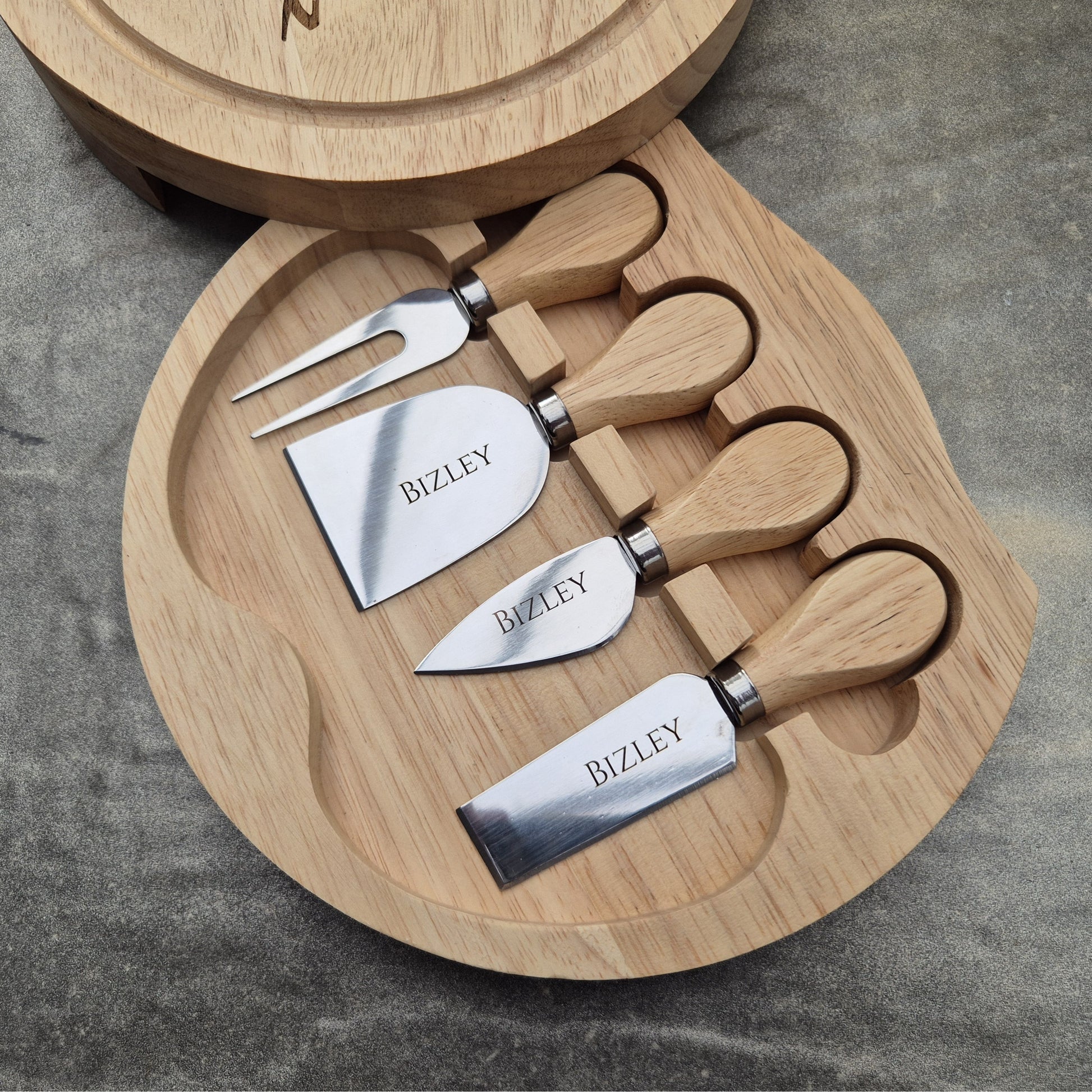 Personalised cheese board with Set of cheese knives with wooden handles and a round wooden board on a gray surface