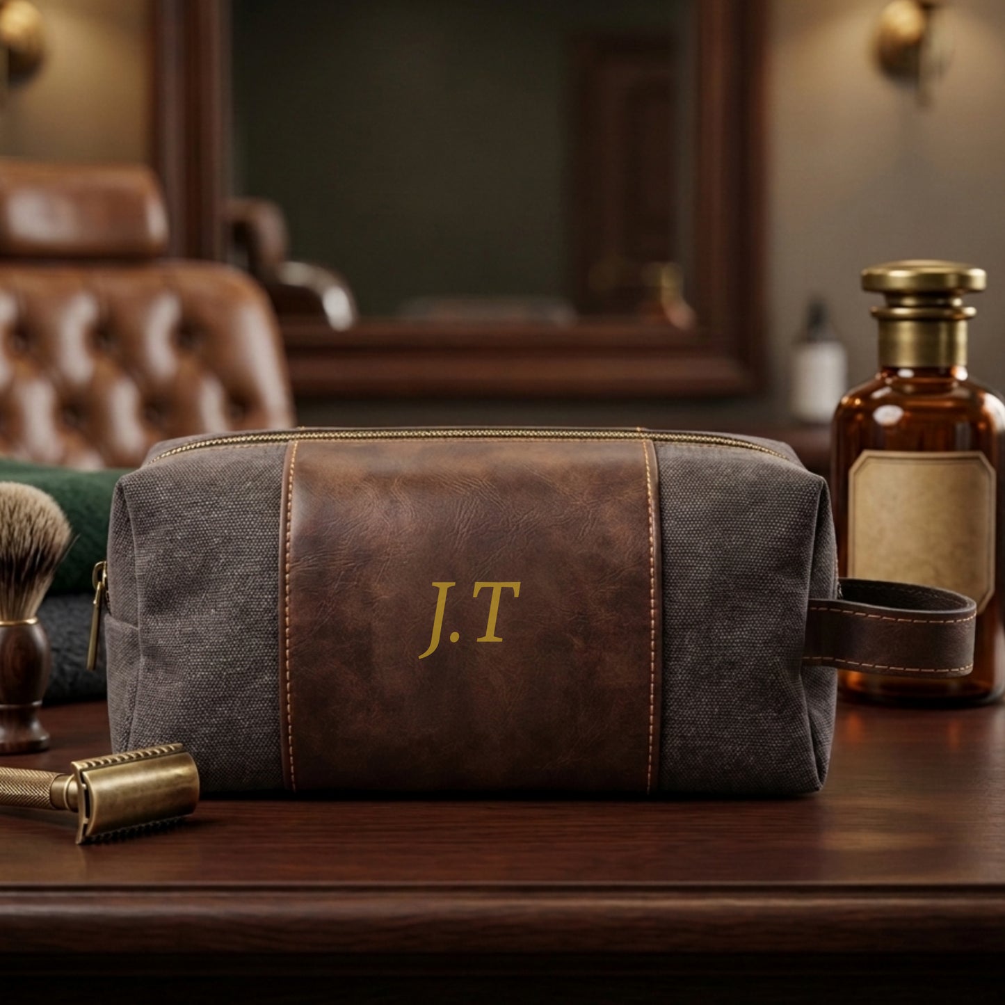 A personalized grooming pouch with a brown faux-leather front panel and gray canvas body, featuring a gold embroidered 'J.T' monogram.