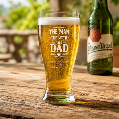 Pilsner Urquell beer bottle with a personalized glass on a wooden table outdoors.