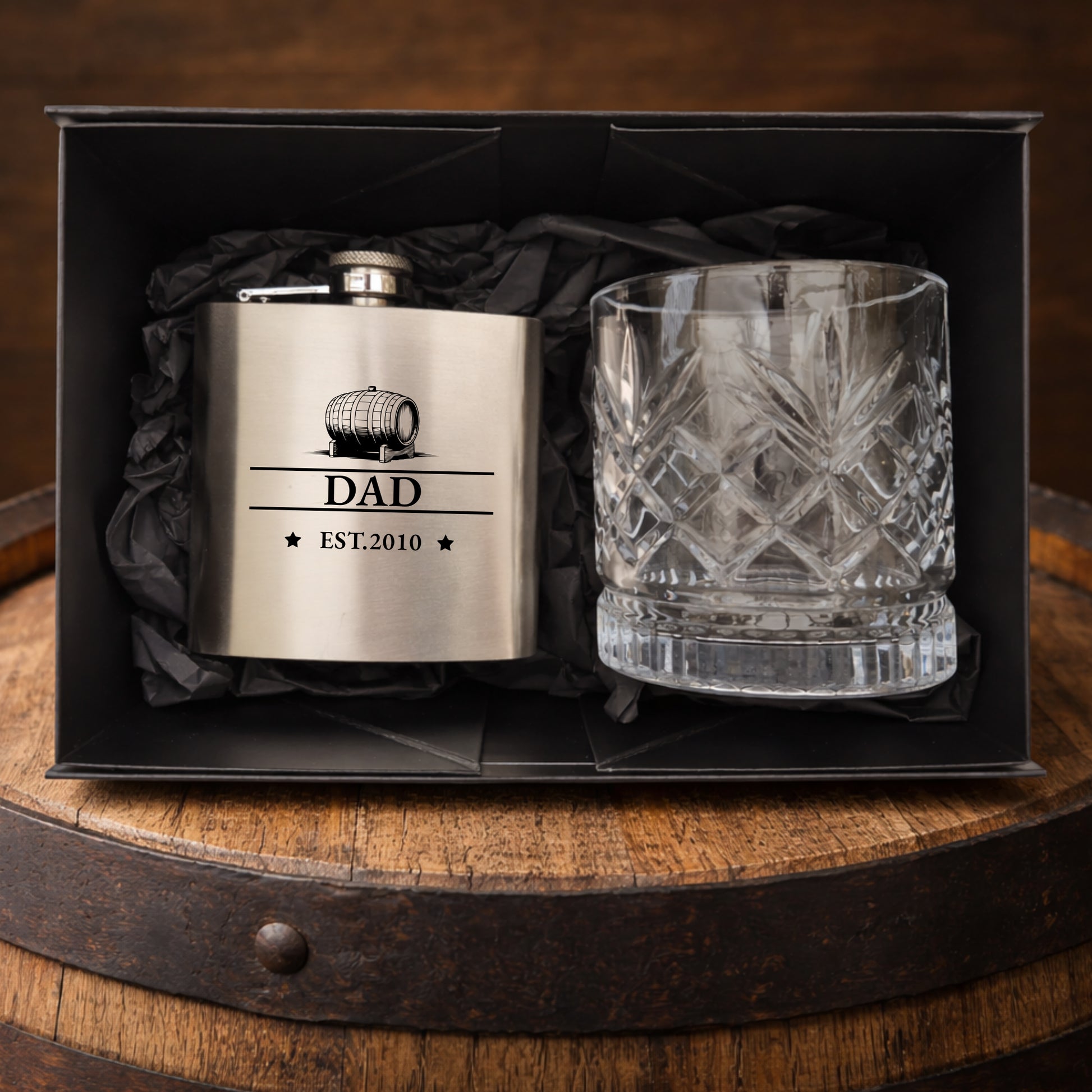 Flask and glass set with 'DAD' engraving in a black box on a wooden barrel.