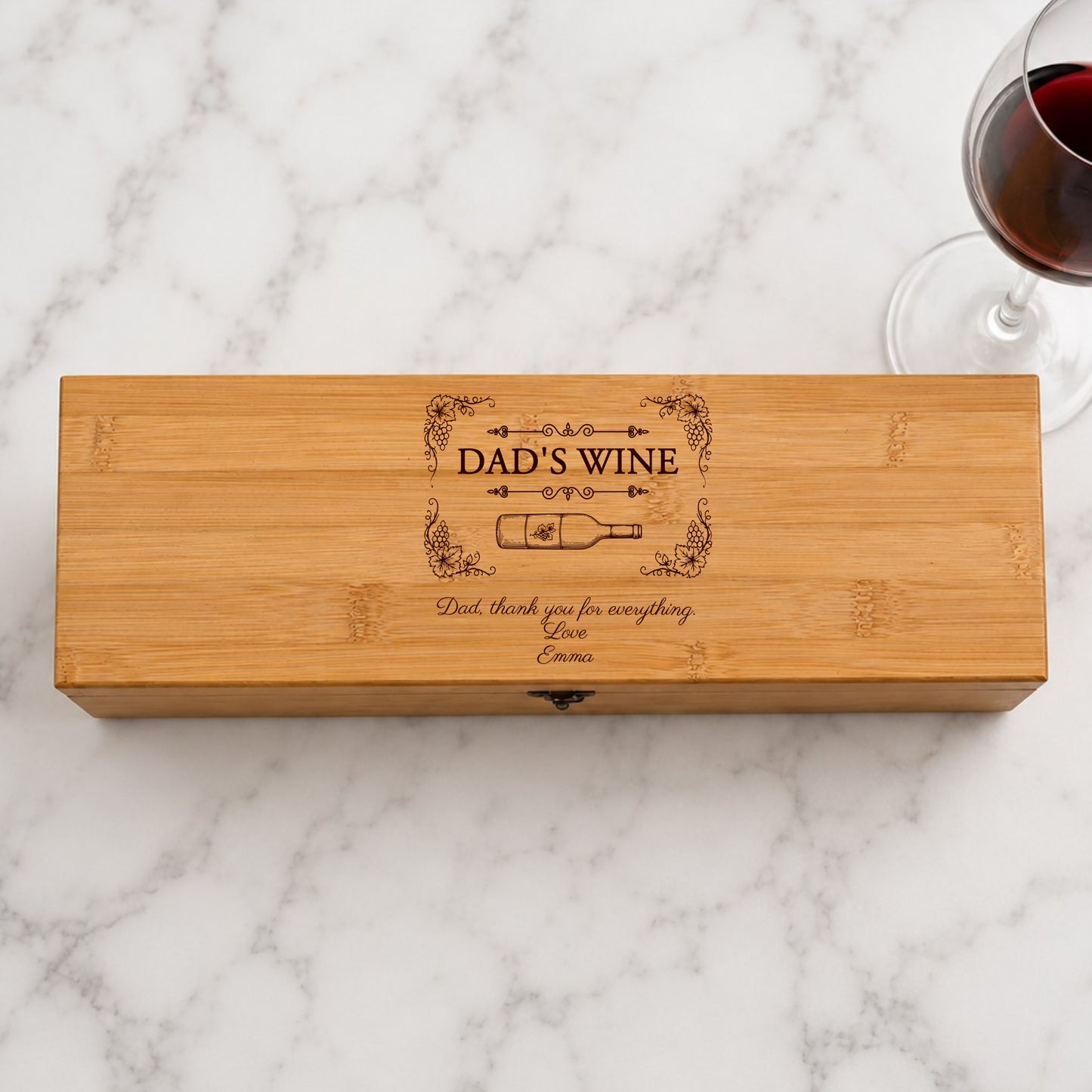 Wooden wine box with 'Dad's Wine' engraving on a marble surface with a glass of red wine.