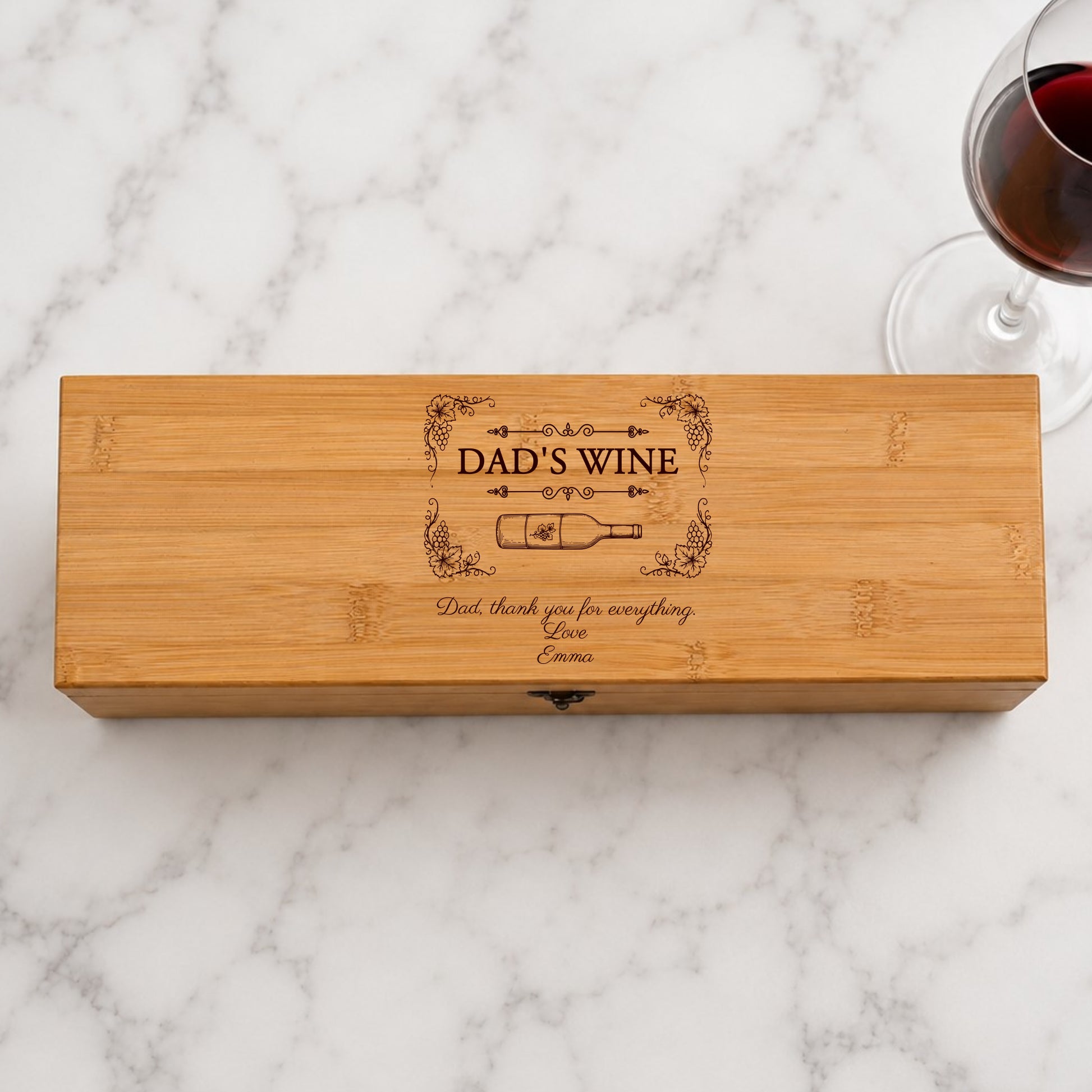 Wooden wine box with 'Dad's Wine' engraving on a marble surface with a glass of red wine.