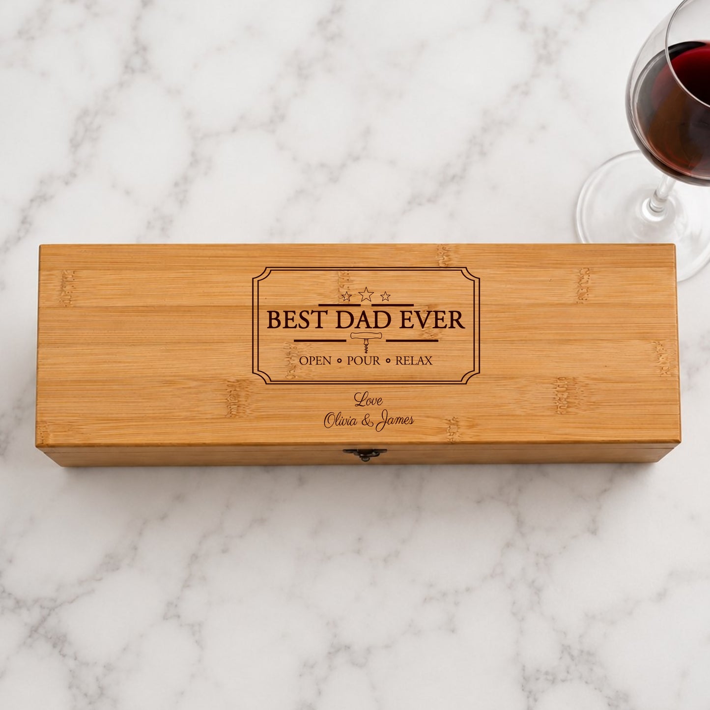 Wooden wine box with 'Best Dad Ever' engraving on a marble surface with a glass of red wine.