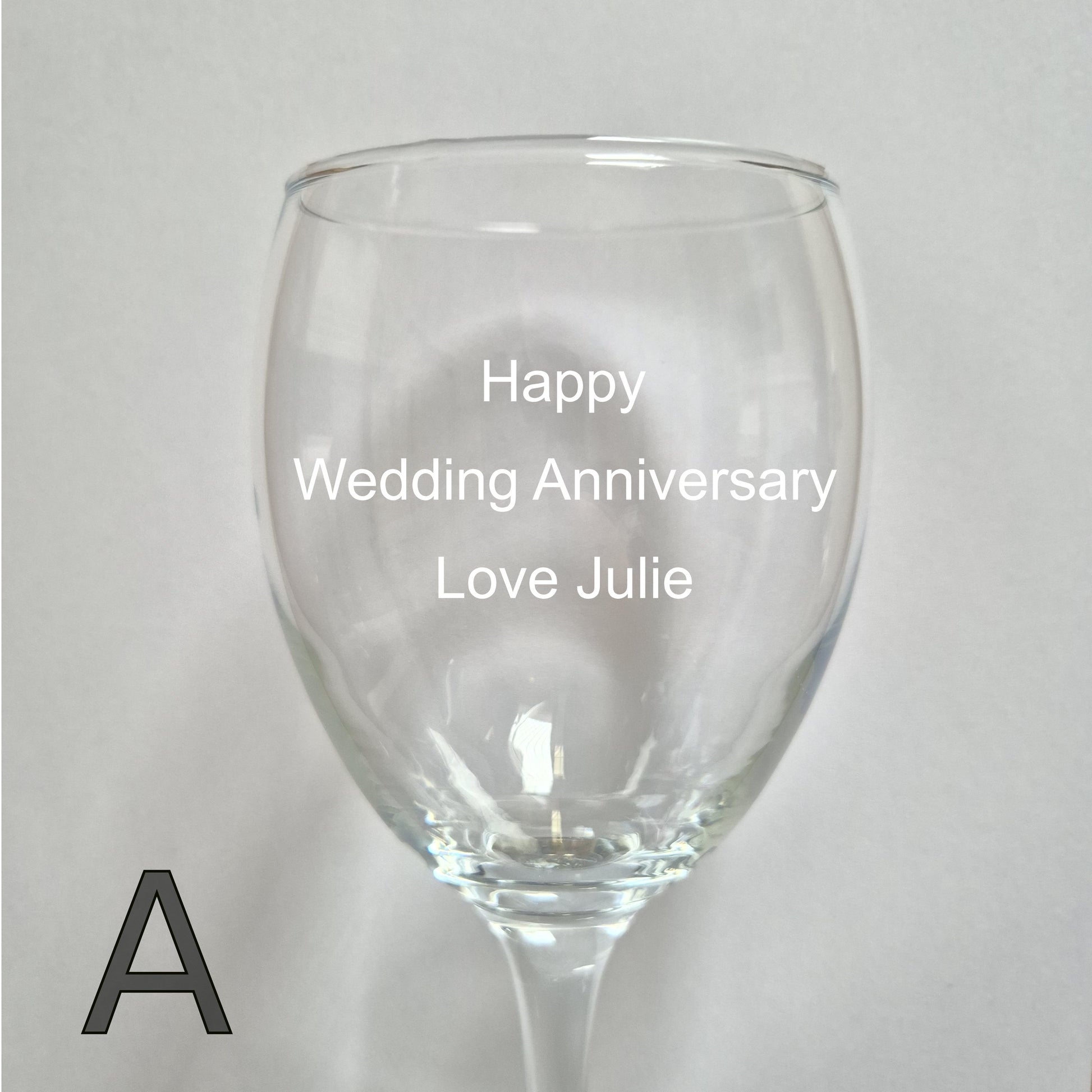 Personalised wine glass with 'Happy Wedding Anniversary Love Julie' text on a light gray background