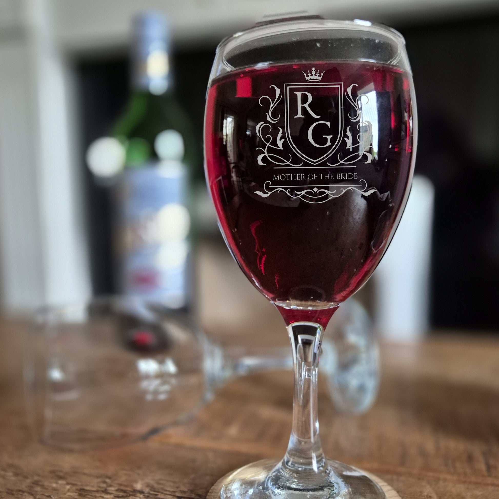 personalised wine glass with logo engraved on the front. glass is filled with red wine on a wooden table.