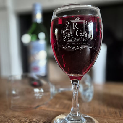 personalised wine glass with logo engraved on the front. glass is filled with red wine on a wooden table.