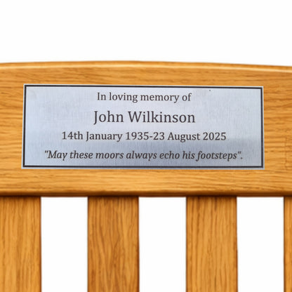 Stainless steel memorial plaque on a wooden bench with engraved text.