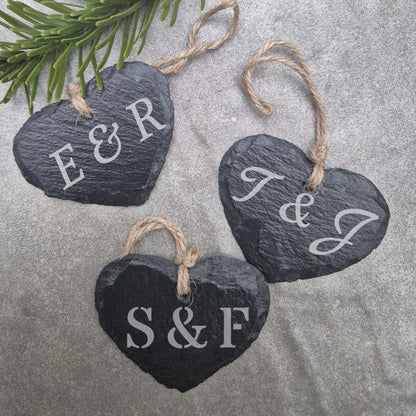 Three slate heart-shaped ornaments with initials on a textured surface.