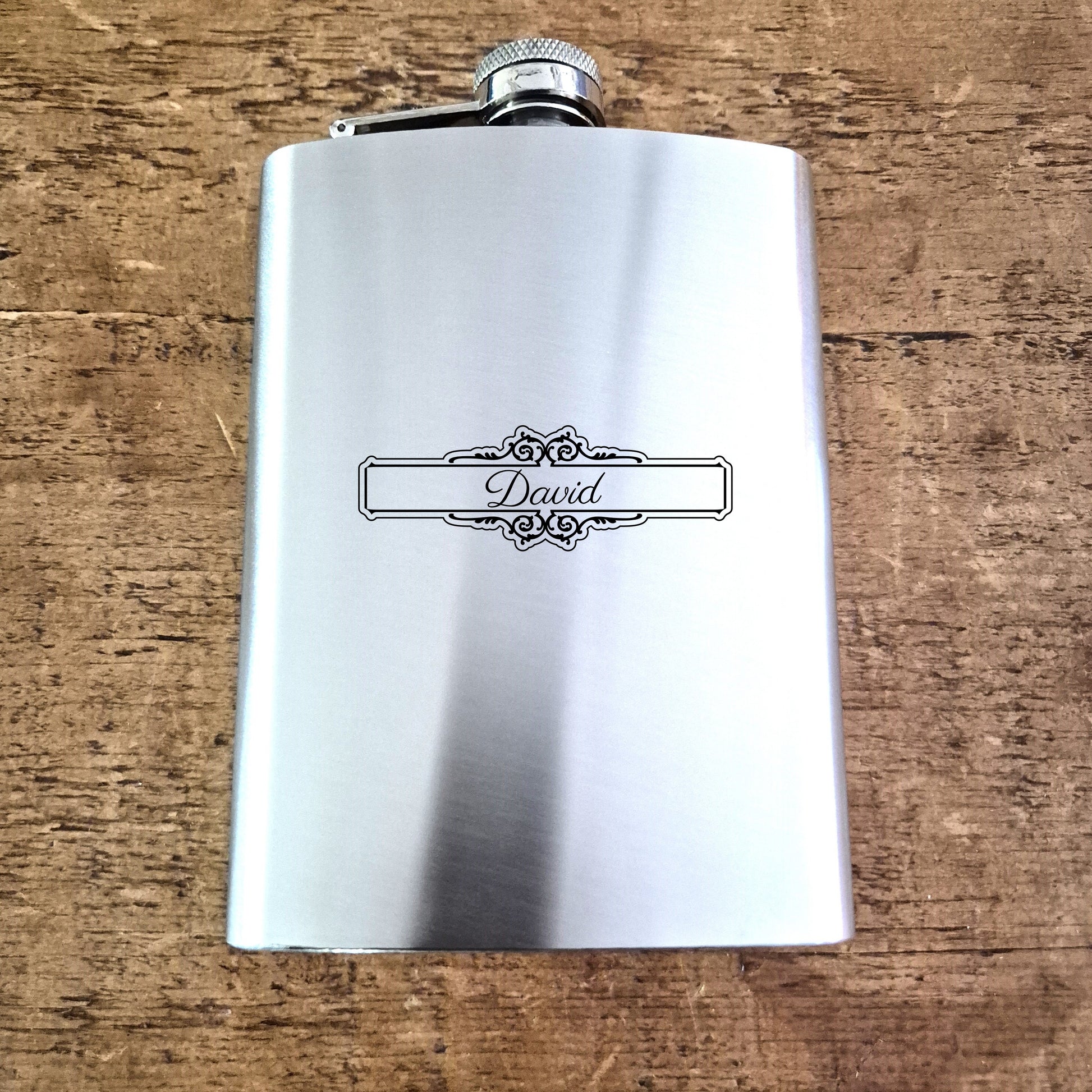 Stainless steel hip flask with 'David' engraving on a wooden surface