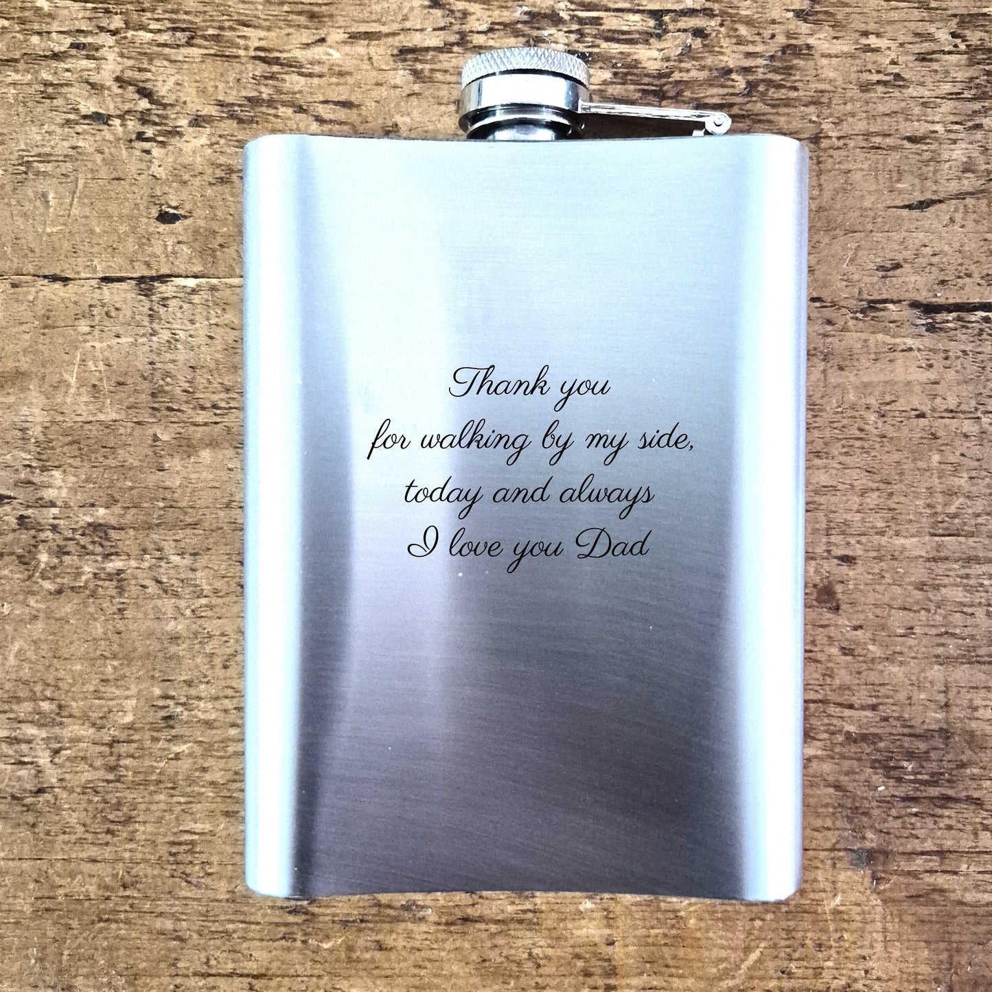 Stainless steel hip flask with engraved message on a wooden surface