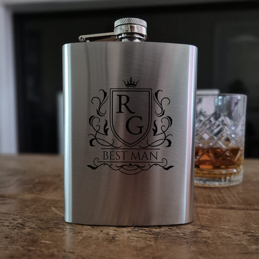 Personalised hip flask Stainless steel  with 'Best Man' engraving on a wooden surface with a glass of whiskey in the background.