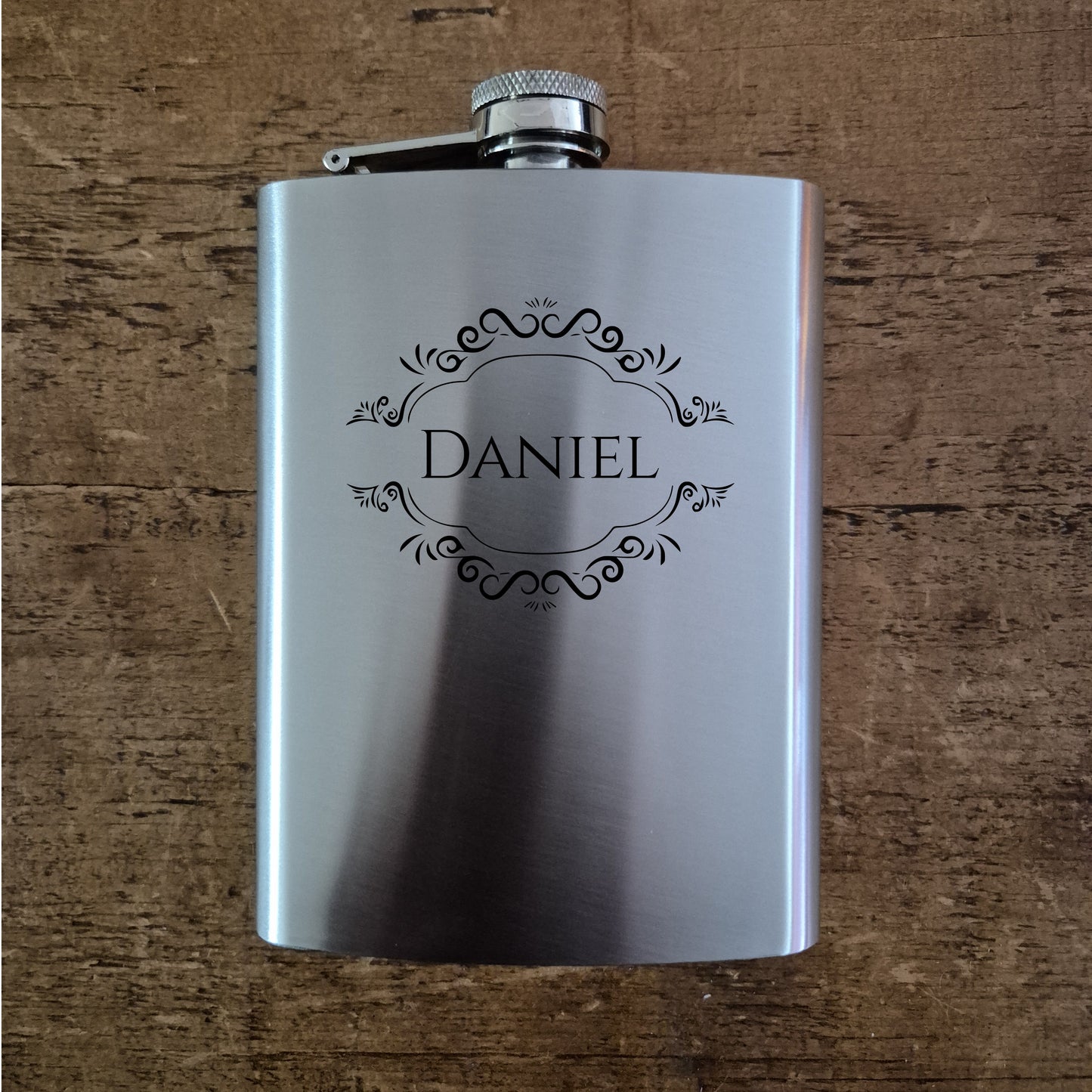 Silver flask with 'Daniel' engraving on a wooden surface