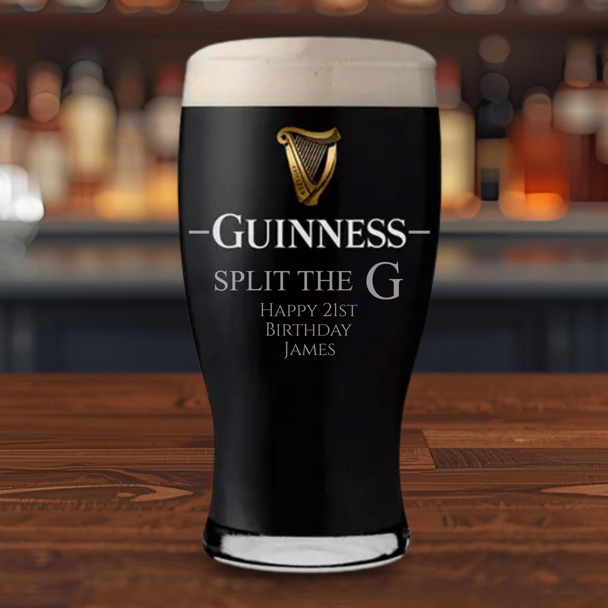 Personalized Guinness pint glass on a bar counter with a blurred bar background. Split the G is engraved on the pint glass along with a birthday message.