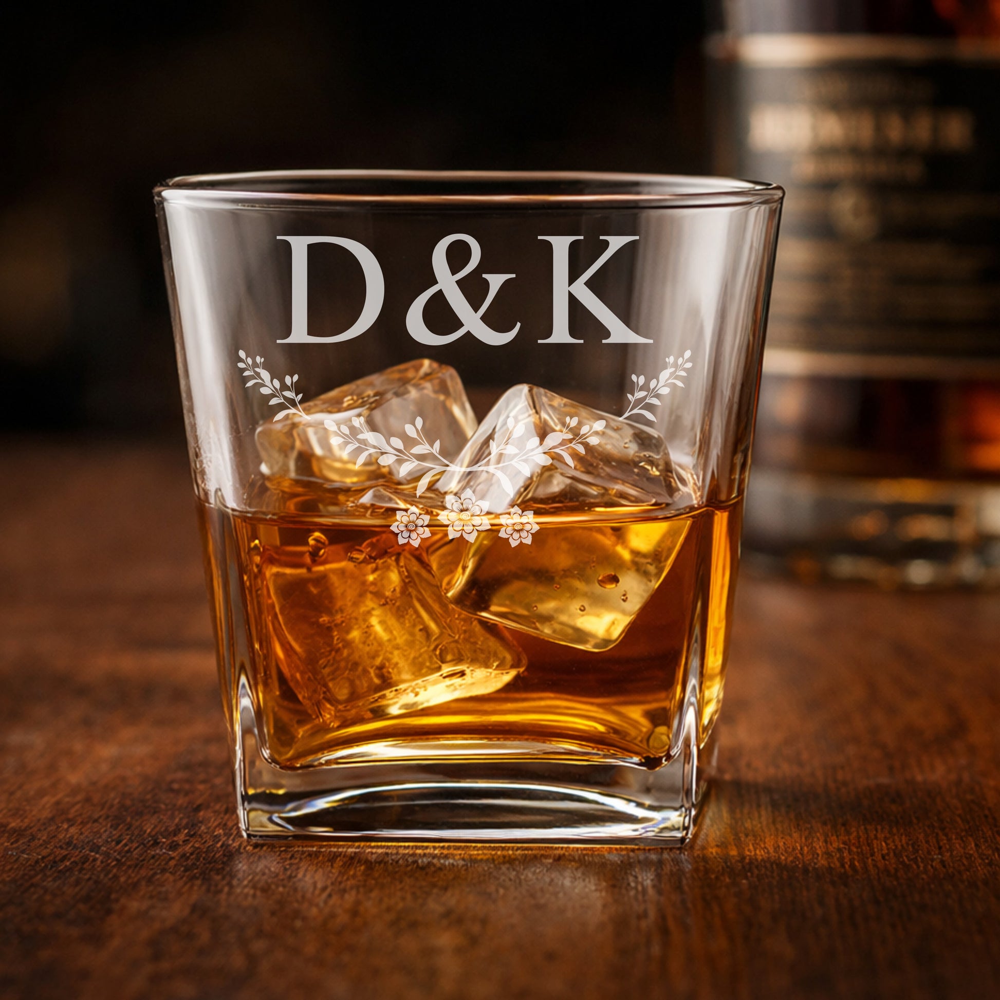Glass of whiskey with ice and 'D&K' engraving on a wooden surface