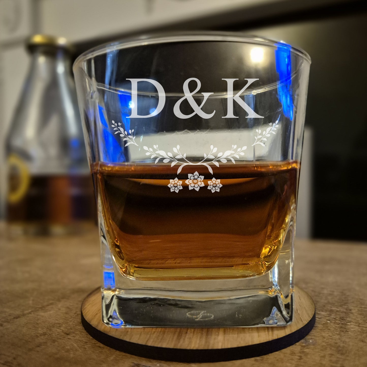 Glass of whiskey with 'D&K' engraving on a wooden coaster.
