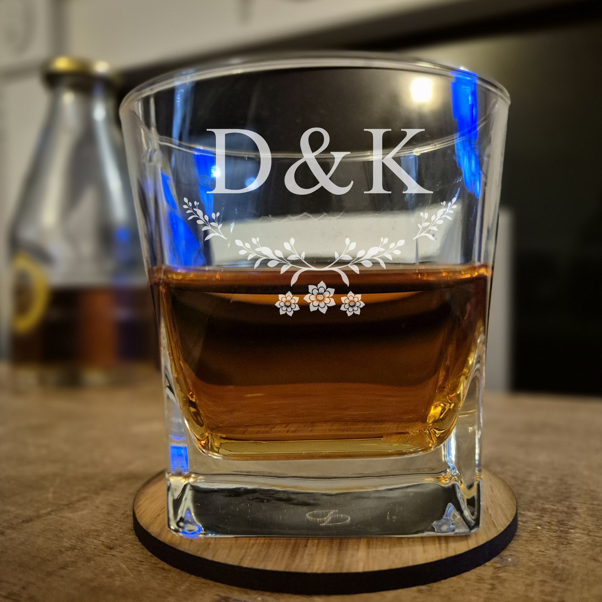 Glass of whiskey with 'D&K' engraving on a wooden coaster.