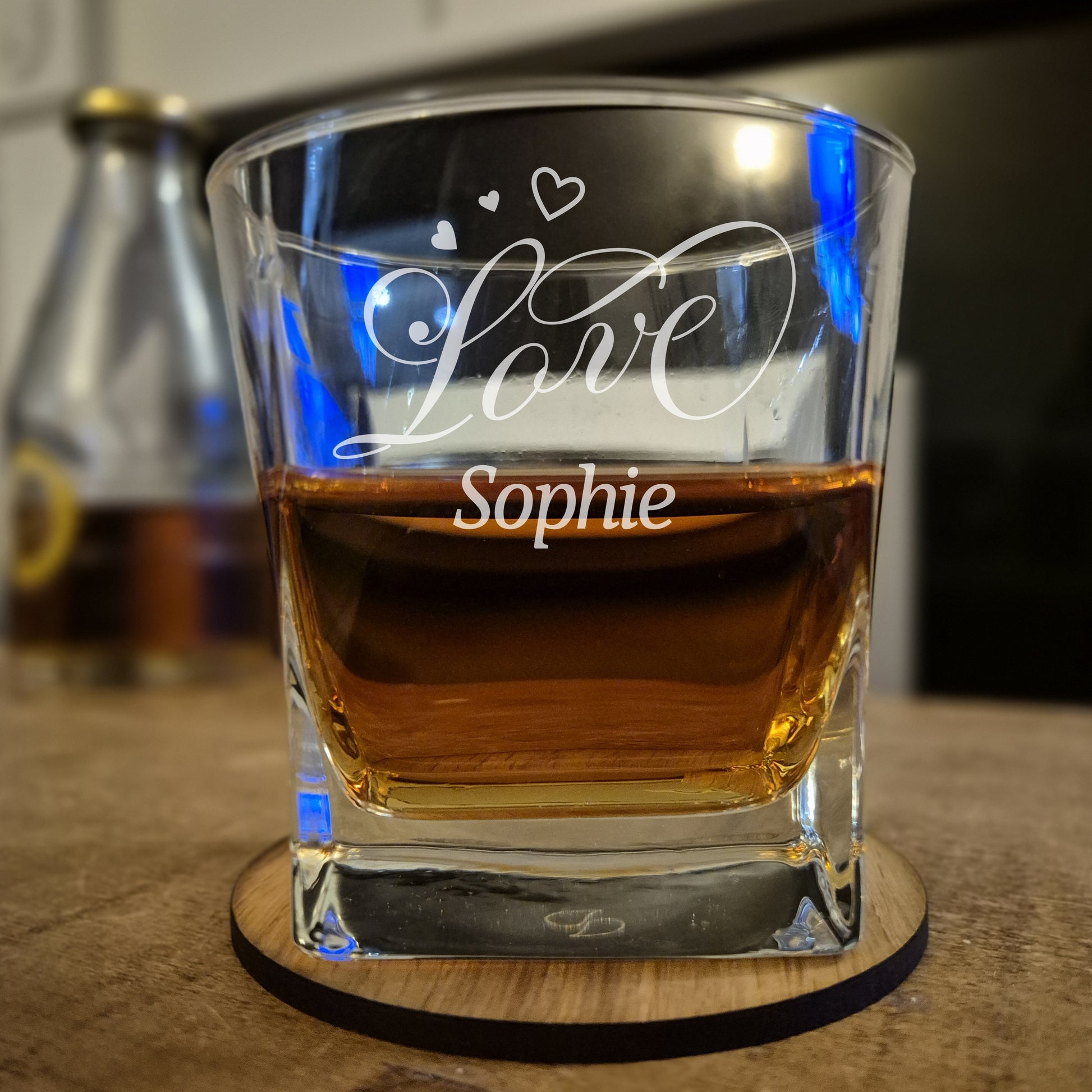 Glass of whiskey with 'Love Sophie' engraving on a wooden coaster.