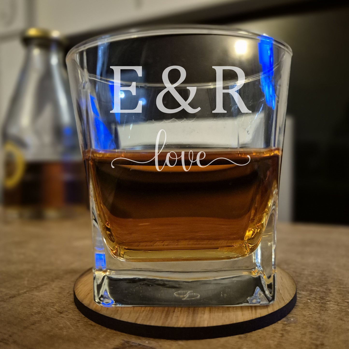 Glass of whiskey with 'E & R love' engraving on a wooden coaster.
