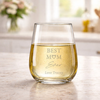 Clear glass stemless wine glass with 'Best Mom Ever' engraving on a light wooden surface.