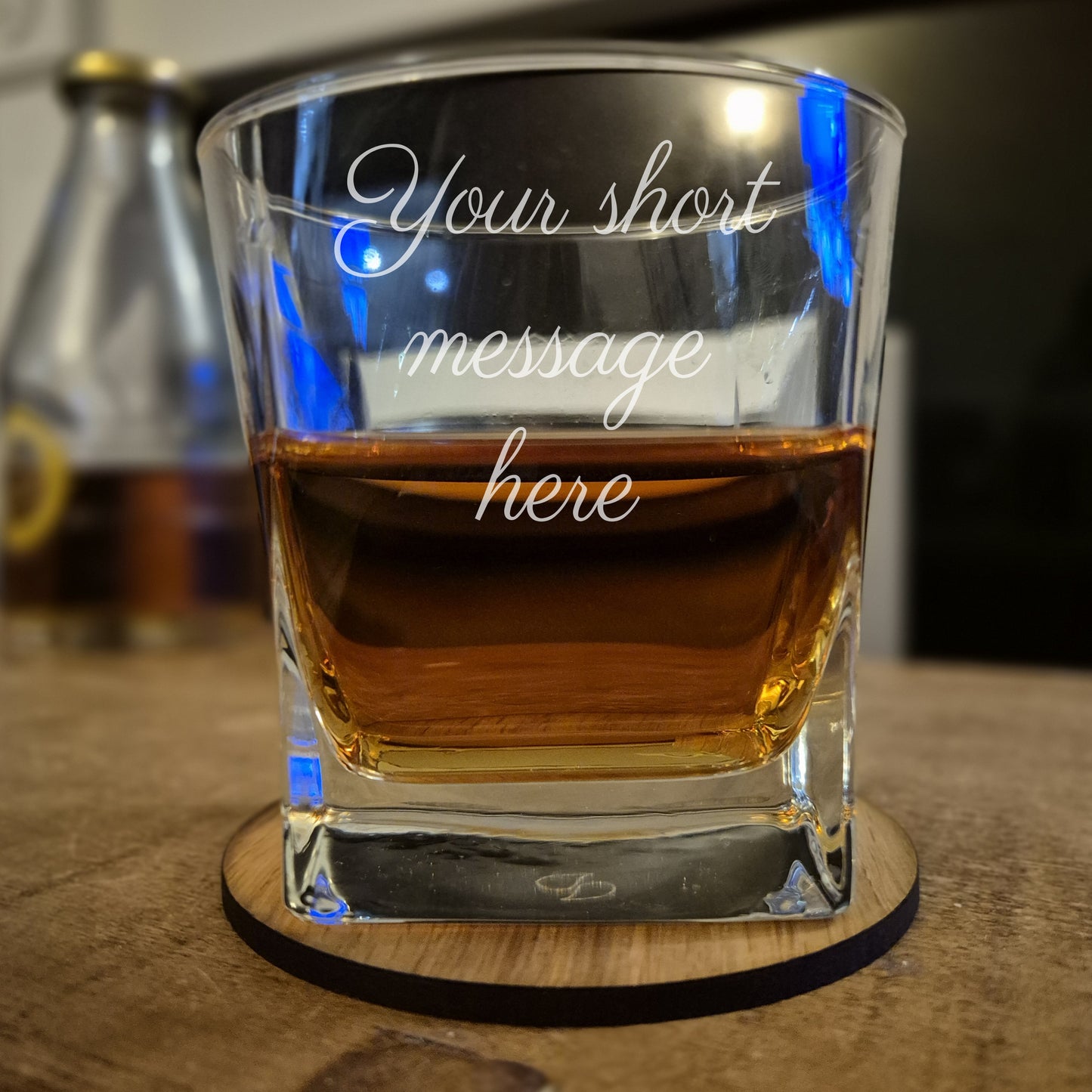 Clear glass with engraved text on a wooden coaster, filled with amber liquid.