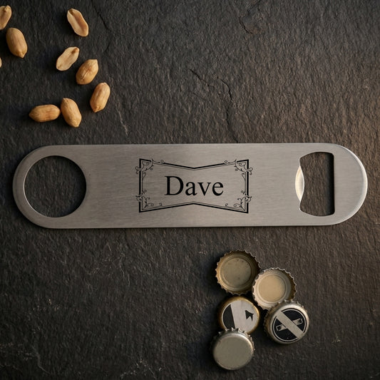 A personalized stainless steel bottle opener engraved with the name 'Dave', displayed on a dark slate background with scattered peanuts and bottle caps.