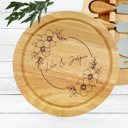 Wooden cheese board with floral design and engraved names on a white wooden surface.