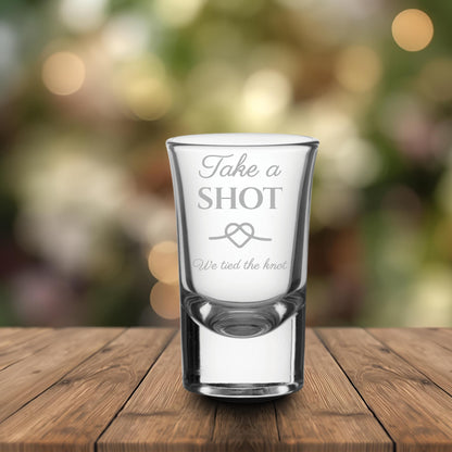 Clear shot glass with engraved text on a wooden surface with a blurred bokeh background