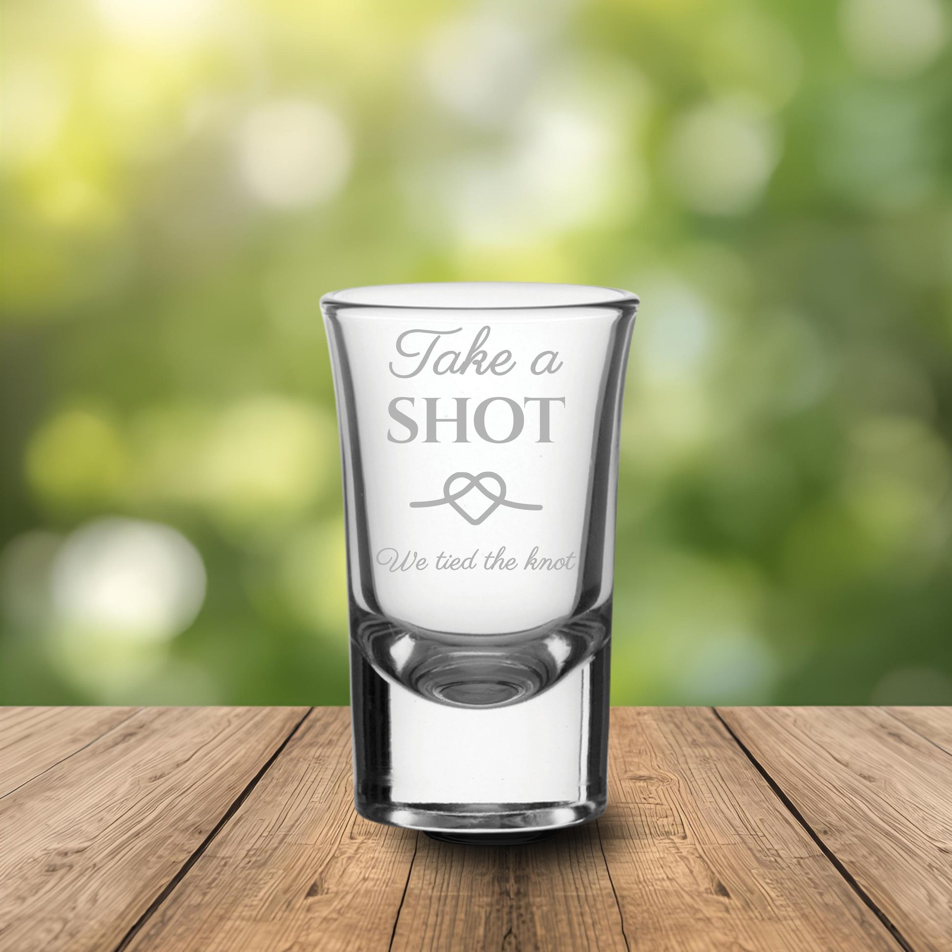 Personalised shot glass with engraved text on a wooden table with a blurred wedding backdrop