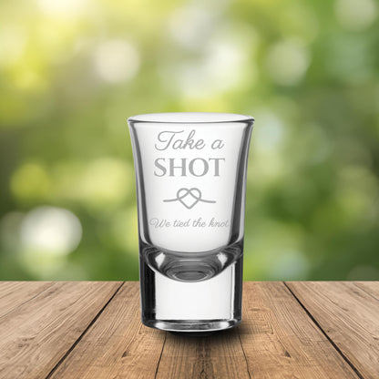 Personalised shot glass with engraved text on a wooden table with a blurred wedding backdrop