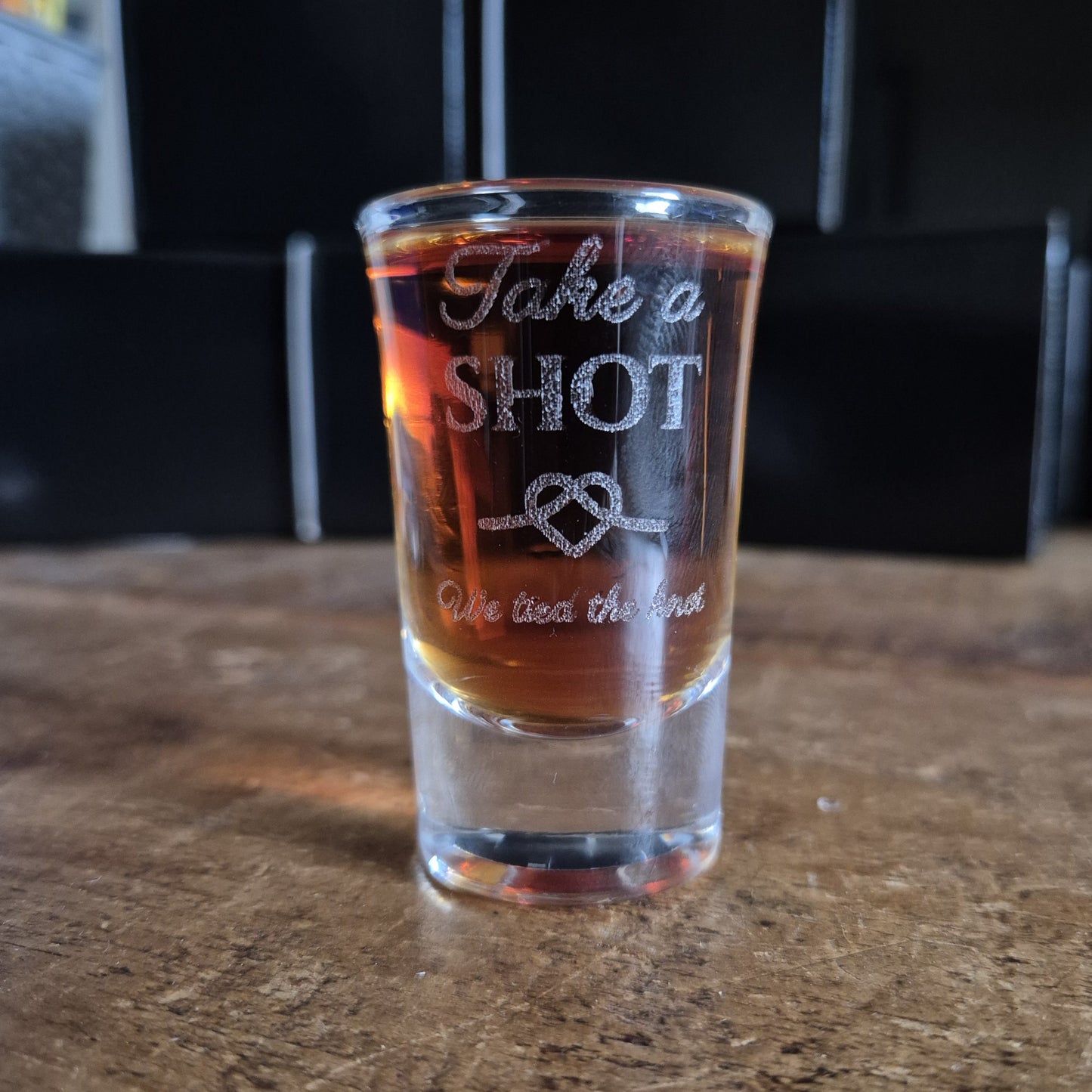 Personalised shot glass with engraved text on a wooden table with a blurred wedding backdrop