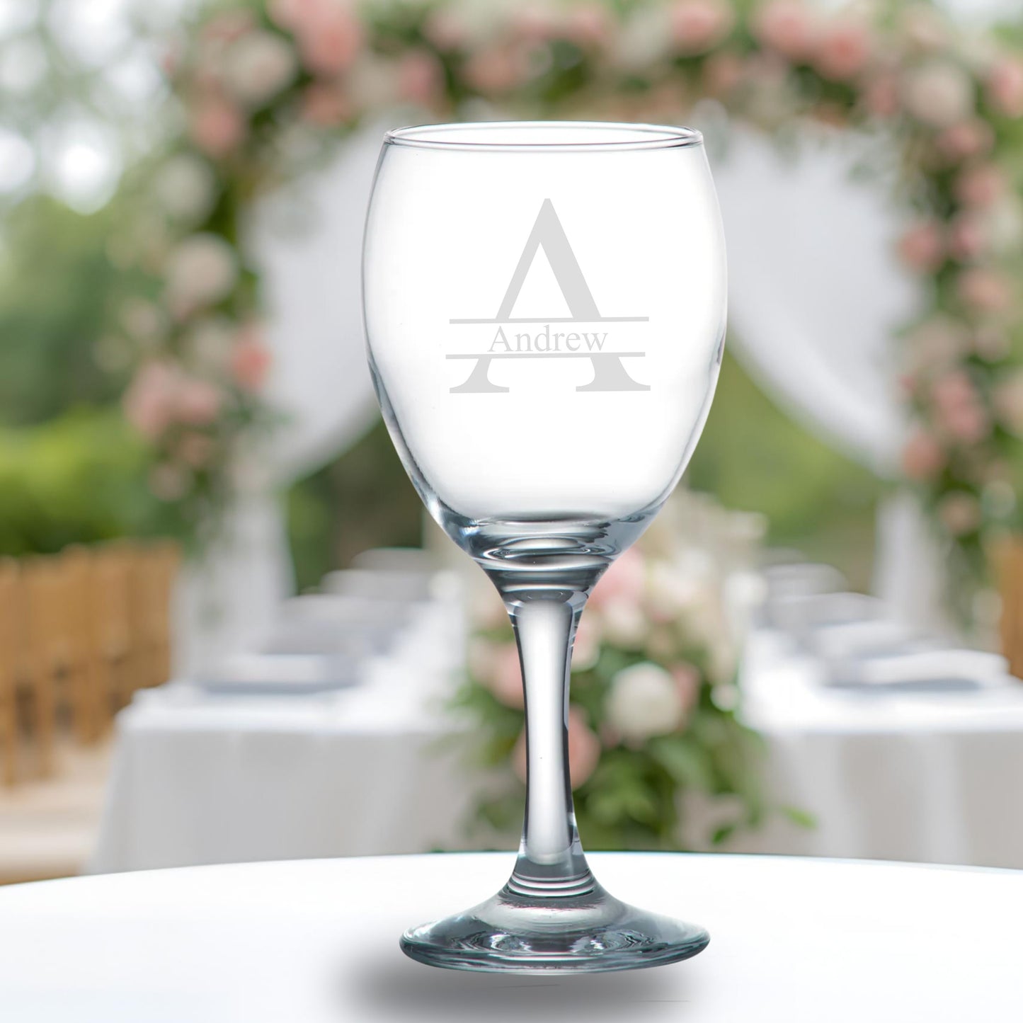 Clear wine glass with engraved 'A' and 'Andrew' on a blurred outdoor background