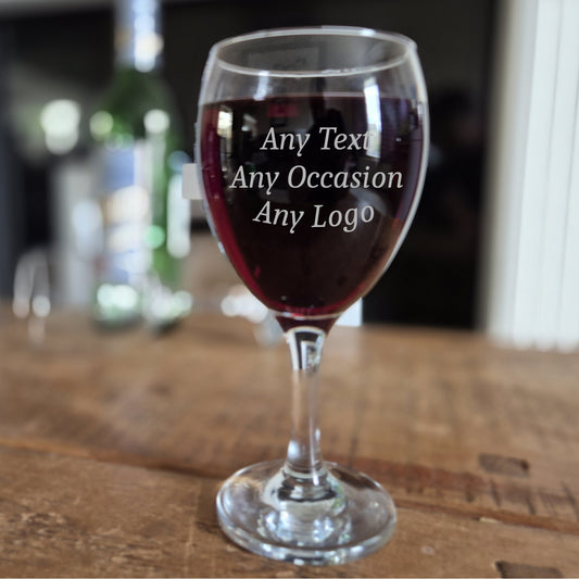 Wine glass with red wine on a wooden table, text engraved 'Any Text Any Occasion Any Logo'.