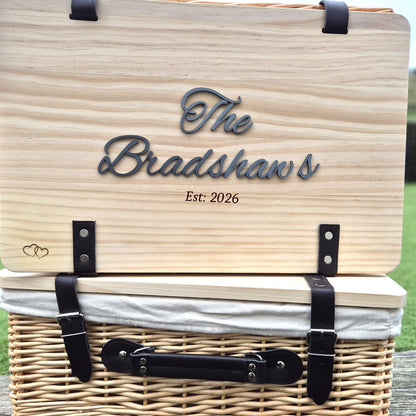 Wooden picnic basket with 'The Bradshaws Est: 2026' engraving on a grassy background
